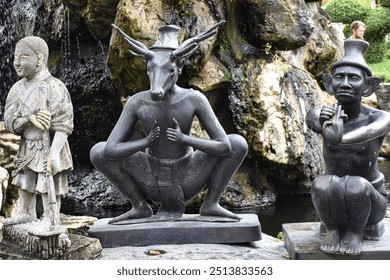 A trio of statues stands against a natural rock formation backdrop. The left statue depicts a person in traditional attire, the center features an anthropomorphic figure with a deer-like head - Powered by Shutterstock