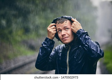 Trip in bad weather. Portrait of young man in drenched jacket in heavy rain.