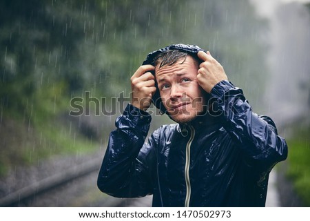 Trip in bad weather. Portrait of young man in drenched jacket in heavy rain.