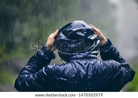Trip in bad weather. Rear view of young man in drenched jacket in heavy rain.