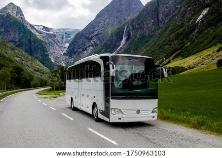 Trip to Norway. Blue ice tongue of Jostedal glacier melts from the giant rocky mountains into the green valley with a lot of waterfalls. Big white tourist bus rides on the road