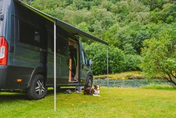 Trip With Pet. Happy Brown Dog Border Collie Travel By Car. Border Collie Dog Sitting Near Car Camping On Green Grass Near Mountain River In Norway. Holiday With Camper And Dog. Doggy Ready For Travel