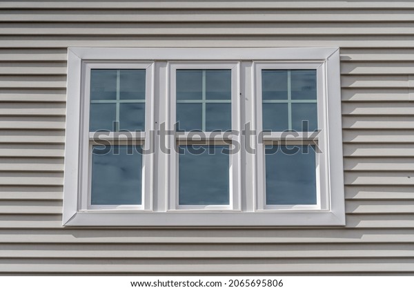 Triple hung window with fixed top sash and\
bottom sash that slides up, sash divided by white grilles a\
surrounded by white elegant frame  horizontal white vinyl siding on\
a new construction\
residence