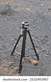 A tripod camera setup on soft sand, capturing the beauty of the natural environment. The contrast between the sturdy tripod and the textured sand creates a balanced outdoor scene.