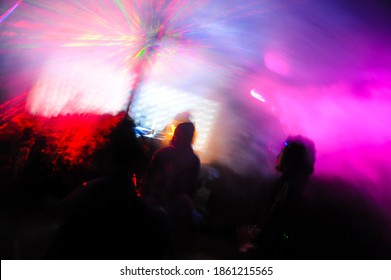Trippy night image with people dancing outdoors in a forest music festival with laser beams in the background.