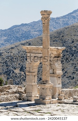 Triumphal arch and honorary column at Upper Agora in ancient city of Sagalassos. Cover page. Scenic mountains of Pisidia at background. Aglasun, Budur, Turkey