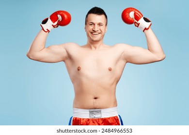 Triumphant boxer in red gloves celebrates victory with a smile, showcasing strength and determination in a blue studio - Powered by Shutterstock