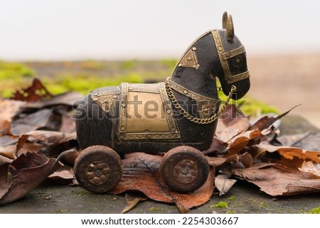 Trojan Horse wooden figure. The horse stands on the fallen autumn leaves in the rainy day outdoors. Concept of Trojan Virus Metaphor.  Close up photography