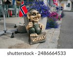 Troll statue holding a Norwegian flag stands beside vibrant flower pots on a charming street in Norway.