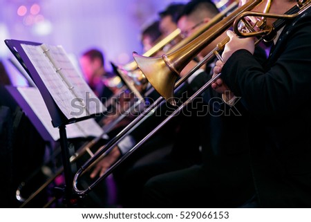 A trombone section playing together in a traditional big band jazz ensemble. Selective focus on the foreground trombone.