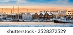 Tromso harbor at sunset in winter, Norway. View of Scandinavian buildings and boats in port of Tromso. Snowy winter landscape in arctic circle town in far northern Norway.