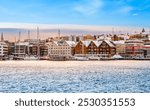 Tromso harbor at sunset in winter, Norway. View of Scandinavian buildings and boats in port of Tromso. Snowy winter landscape in arctic circle town in far northern Norway.