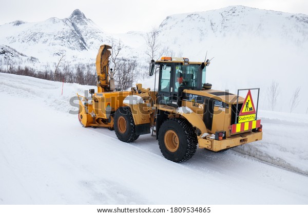 Tromso, Norway, January 20 2020:Snow plow truck\
clearing icy road after winter snowstorm blizzard for vehicle\
access\
Snowblower clears snow-covered streets producing a plume of\
snow. Winter landscape