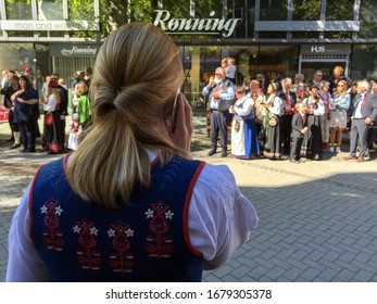 TRONDHEIM, NORWAY - MAY 17, 2019: Back View Of A Blonde Woman Wearing A Bunad Talking On The Phone While Waiting For The Constitution Day School Children Parade To Pass. 