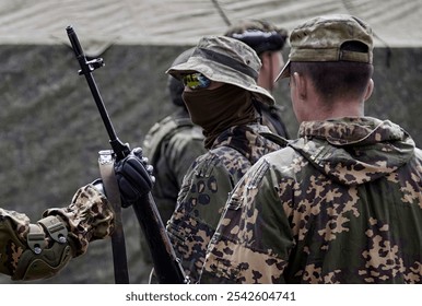 Troops in tactical clothing gather at a training site, discussing plans and checking equipment as day breaks. - Powered by Shutterstock