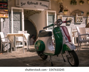 Tropea/Italy - 10/05/2019: Vespa motorbike in colors of Italian flag infront of traditional restaurant and pizzaria with lettering in Tropea, Calabria, Italy