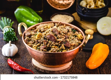 "Feijão tropeiro", typical Brazilian food, in copper pot, rustic cuisine, with ingredients and vegetables in the background.