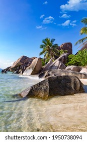 Tropischer Strand mit Palmen, Felsen, weißem Sand und blauem Himmel, berühmter Anse Source d'argent auf La Digue, Inseln der Seychellen