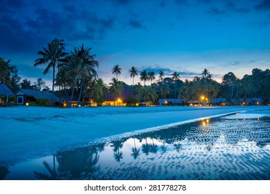 Tropical beach with palm trees and resort lights at night, low tide, on Bintan island, Indonesia