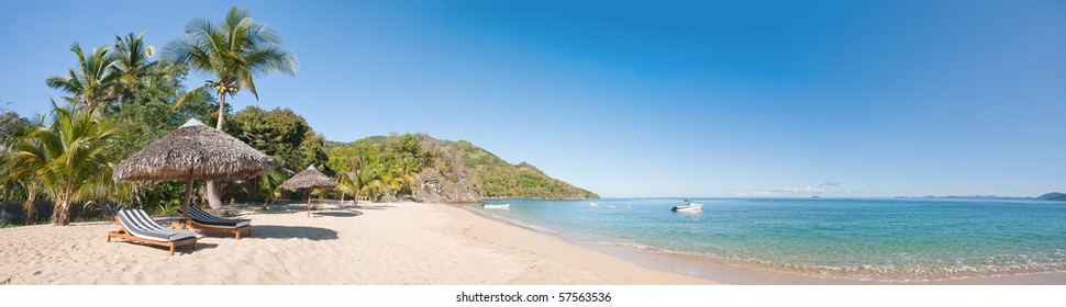 Tropical beach panorama with deckchairs, umbrellas, boats and palm tree