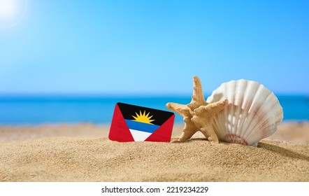 Tropical Beach With Seashells And Antigua And Barbuda Flag. The Concept Of A Paradise Vacation On The Beaches Of Antigua And Barbuda.