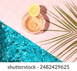 Tropical cocktail with lemon slice, palm leaf  on the edge of pool. Minimal summer drink composition. Flat lay.