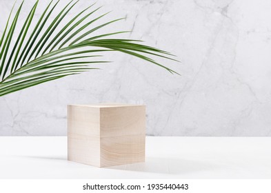 Conception tropicale pour la présentation et l'affichage des produits - podium cubique en bois avec feuille de palmier verte, lumière du soleil et ombre sur table en bois blanc, mur en marbre à la lumière du soleil.