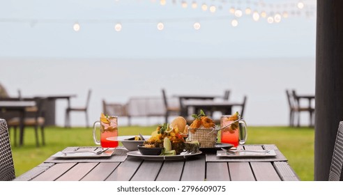 Tropical dinner table featuring pineapple fried rice and cocktails sitting at beachfront restaurant, evening string lights and ocean view, romantic dining, luxury travel lifestyle.