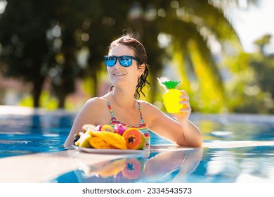 Tropical fruit plate at swimming pool. Young woman eating mango, pineapple, orange and drinking fresh juice on summer vacation at exotic island. Healthy nutrition. Beach holiday and swim fun. - Powered by Shutterstock