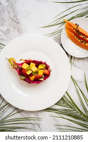 Tropical Fruit Salad Served In Half Dragon Fruit. Top View. Summer Salad On White Plate On Table. Healthy Breakfast, Food Concept. Flat Lay. Vertical Shot.