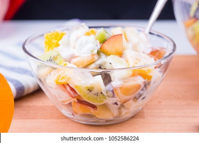 Tropical fruit salad with yoghurt in a glass cup on a wooden table - fruit diet