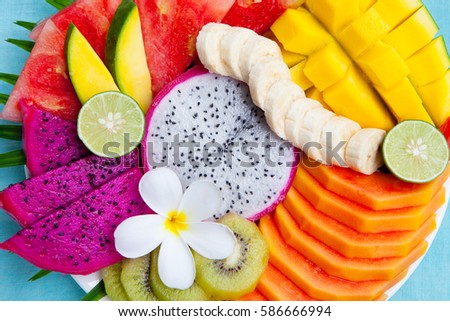 Tropical fruits assortment on a white plate with palm leaf. Blue background. Top view. Copy space.