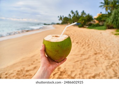 Tropical green coconut in hand with straw on ocean sandy shore - Powered by Shutterstock