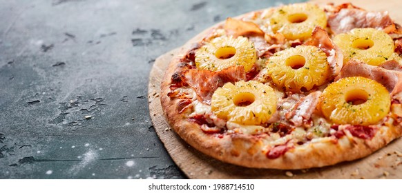 Tropical Hawaiian pizza with pineapple slices and ham on an oven-fired pastry base served whole on a board in a panorama banner with copyspace