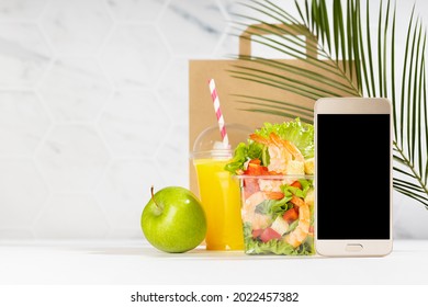 Tropical Lunch Set Of Orange Juice, Sea Food Shrimp Salad In Box, Blank Phone, Packet In White Restaurant Interior, Palm Leaf. Mockup For Advertising For Delivery Service, Take Away Restaurant.