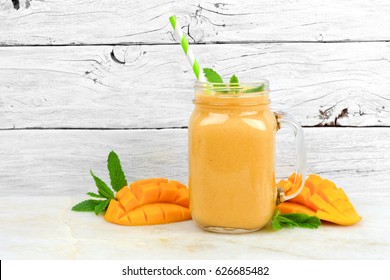 Tropical mango coconut smoothie in a mason jar glass, on a rustic white wood background