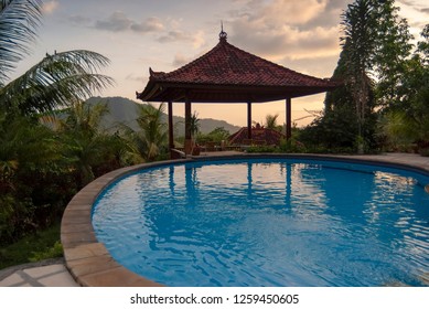 Tropical Resort Swimming Pool on the Island of Bali at Sunset. Gorgeous azure blue swimming pool with an Indonesian bale in the background during a beautiful sunset. 