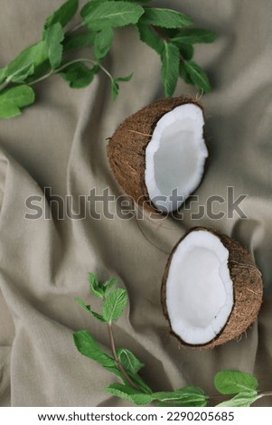 tropical ripe coconut halves with white flesh and green mint leaves on a light beige fabric. for banners, screensavers, postcards, labels, signboards, napkins, lunchboxes, etc.