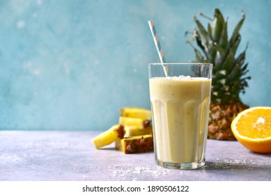 Tropical smoothie with pineapple, banana, coconut and orange in a tall glass on a light blue slate, stone or concrete background.