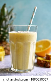 Tropical smoothie with pineapple, banana, coconut and orange in a tall glass on a light blue slate, stone or concrete background.
