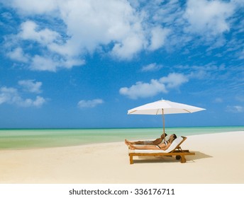 Tropical summer beach holiday couple relax in the sun on their deck chairs 