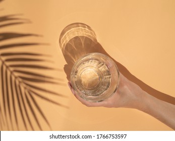 Tropical summer drinks and beach bar concept. Palm leaf shadow and female hand holds glass of water over beige background - Powered by Shutterstock