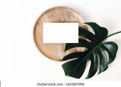 Tropical summer stationery mock-up scene. Blank business card, wooden tray, green monstera leaf isolated on white table background. Summer branding styled photo, web banner. Flat lay, top view