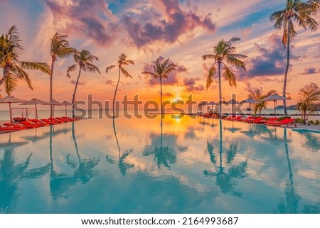 Tropical sunset over outdoor infinity pool in summer seaside resort, beach landscape. Luxury tranquil beach holiday, poolside reflection, relaxing chaise lounge romantic colorful sky, chairs umbrella