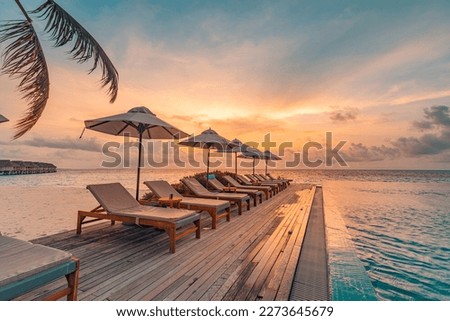 Tropical sunset over outdoor infinity pool in summer seaside resort, beach landscape. Luxury tranquil beach holiday, poolside reflection, relaxing chaise lounge romantic colorful sky, chairs umbrella

