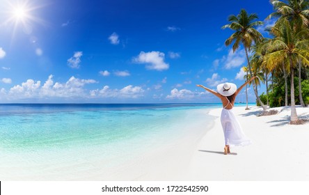 A tropical travel concept banner with copy space showing a woman in white dress walking down a paradise beach with palm trees and turquoise sea