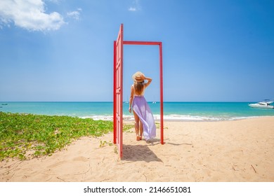 Tropical travel vacation. Traveler woman walks out in red door on the sandy beach to turquoise sea, toward vacation and relaxation in sunny Asia. Carefree girl tourist in swimwear in Asian destination - Shutterstock ID 2146651081