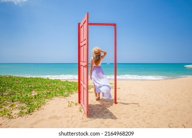 Tropical Travel Vacation. Traveler Woman Walks Out In Red Door On The Sandy Beach To Turquoise Sea, Toward Vacation And Relaxation In Sunny Asia. Carefree Girl Tourist In Swimwear In Asian Destination