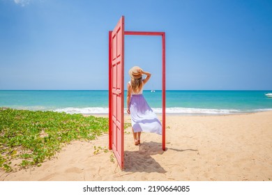 Tropical Travel Vacation. Traveler Woman Walks Out In Red Door On The Sandy Beach To Turquoise Sea, Toward Vacation And Relaxation In Sunny Asia. Carefree Girl Tourist In Swimwear In Asian