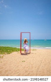 Tropical Travel Vacation. Traveler Woman Walks Out In Red Door On The Sandy Beach To Turquoise Sea, Toward Vacation And Relaxation In Sunny Asia. Carefree Girl Tourist In Swimwear In Asian Destination